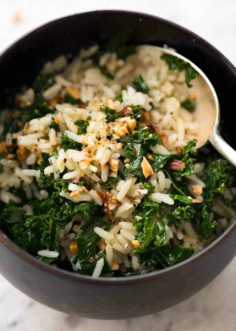 Garlic Butter Rice with Kale in a dark brown bowl with a silver spoon, ready to be eaten.
