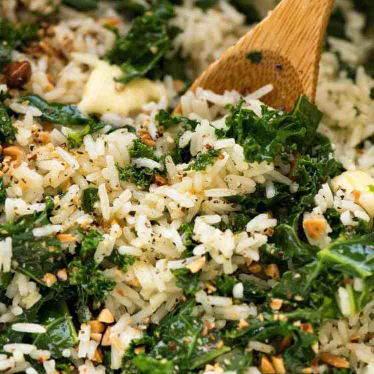 Close up of Garlic Butter Rice with Kale recipe in a pot with a wooden spoon, fresh off the stove ready to be served.