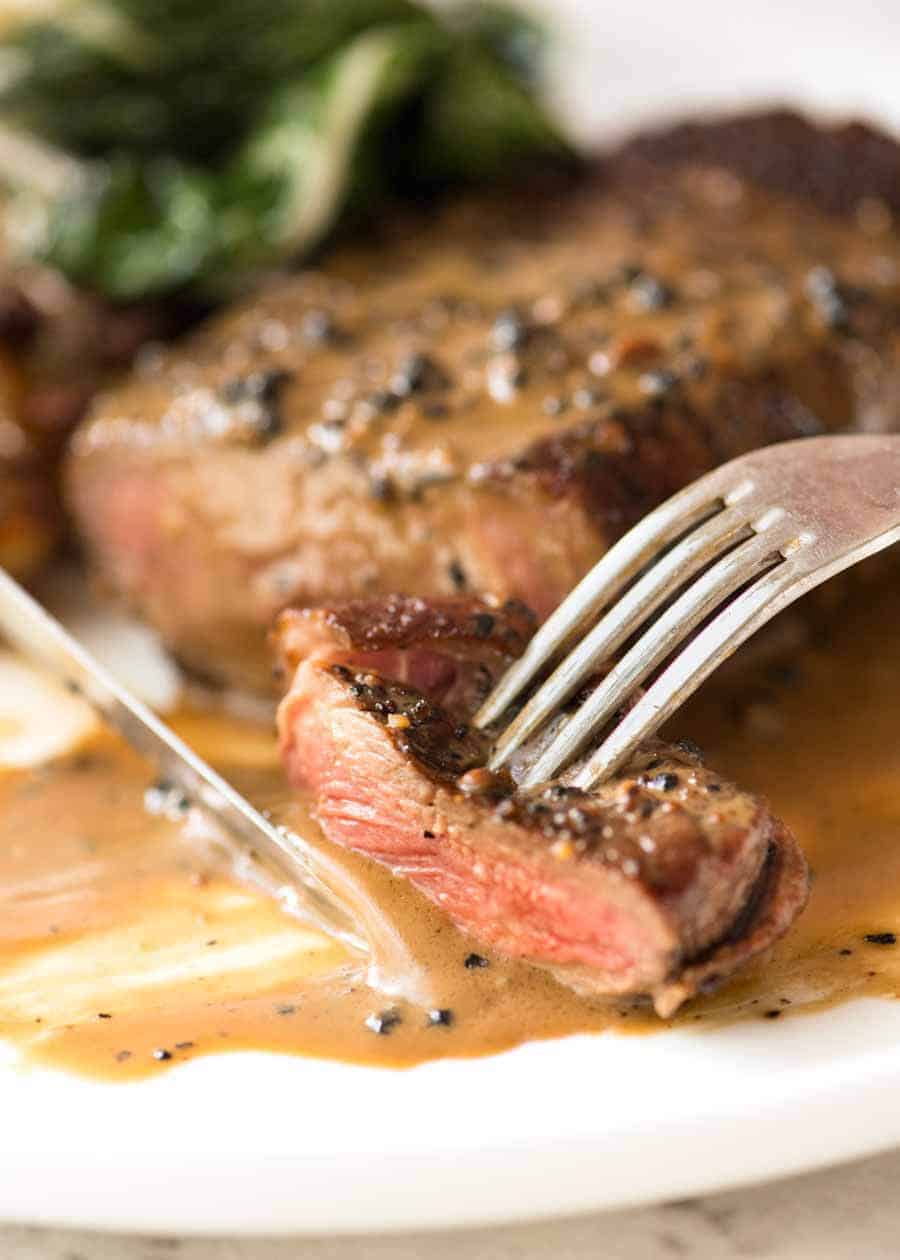 Close up of fork and knife eating a piece of Steak with Creamy Peppercorn Sauce