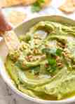 Avocado Dip in a rustic white bowl being scooped up with a corn chip