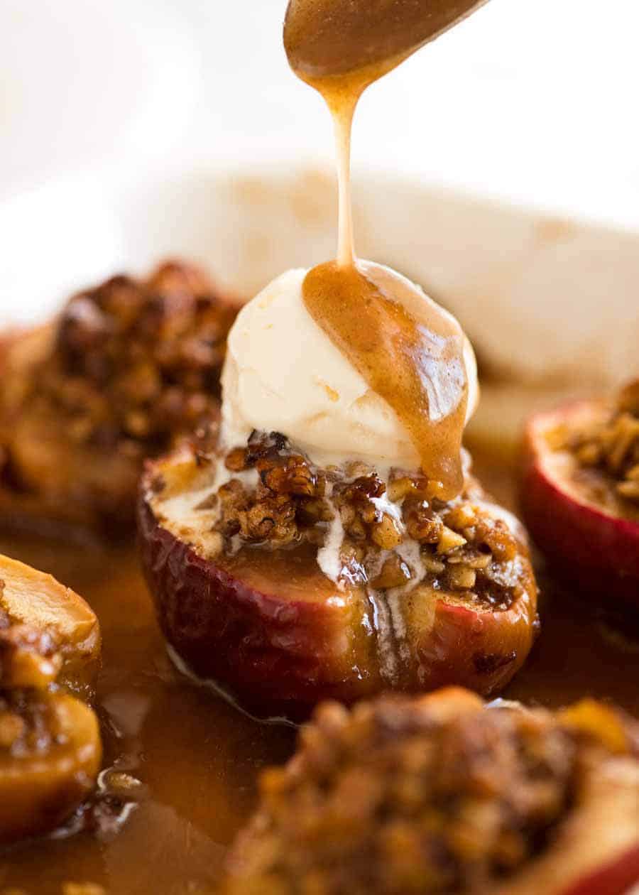 Close up of caramel sauce being drizzled over Baked Apples with ice cream on top in a baking dish, fresh out of the oven.