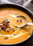 Close up of Carrot Soup in a rustic black bowl being scooped up with a spoon.