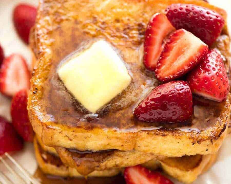 Close up of French Toast doused with maple syrup, a melting pat of butter and strawberries.