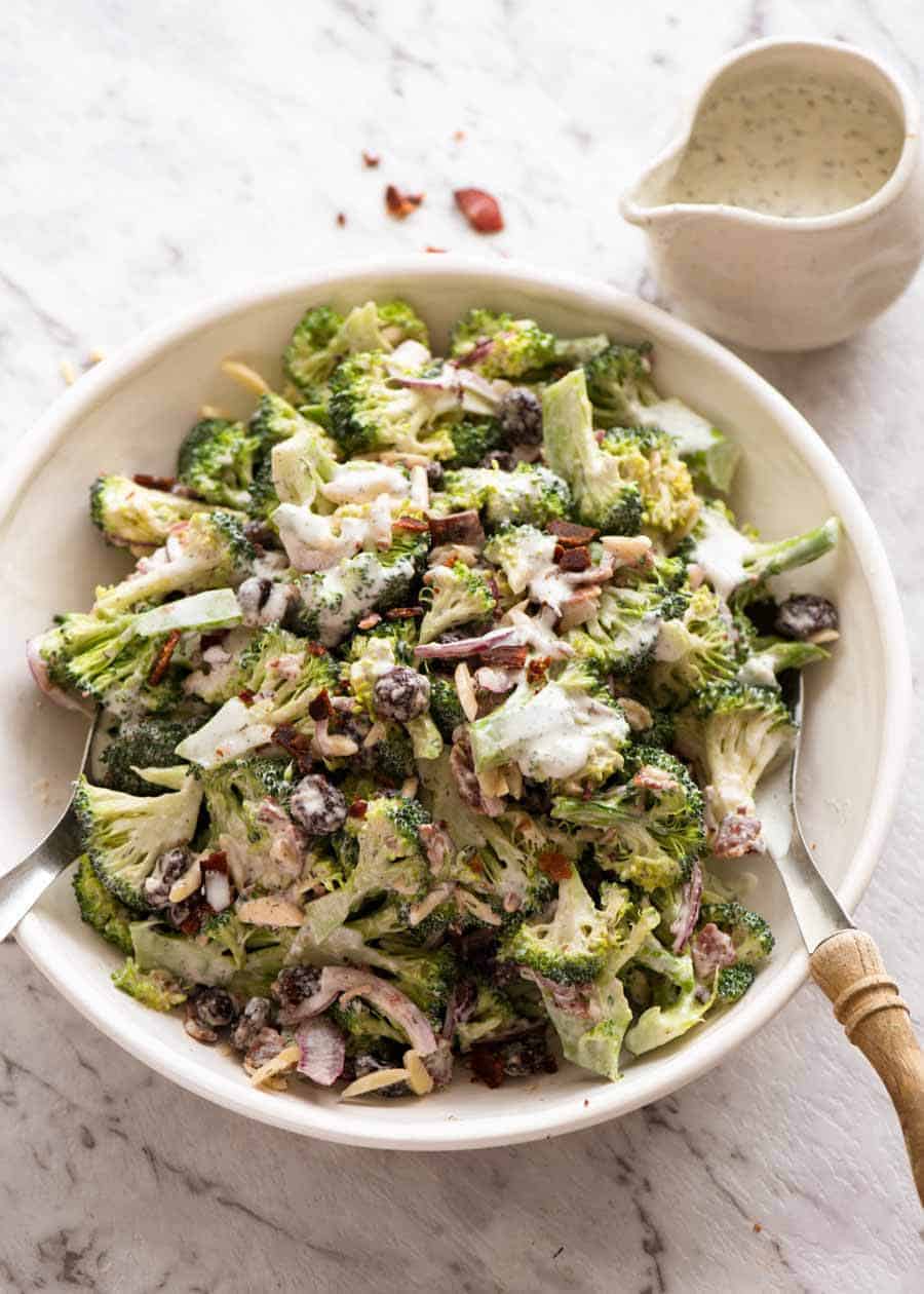 Broccoli Salad with Lighter Creamy Dressing in a white bowl with a jug of dressing on the side, ready to be served.