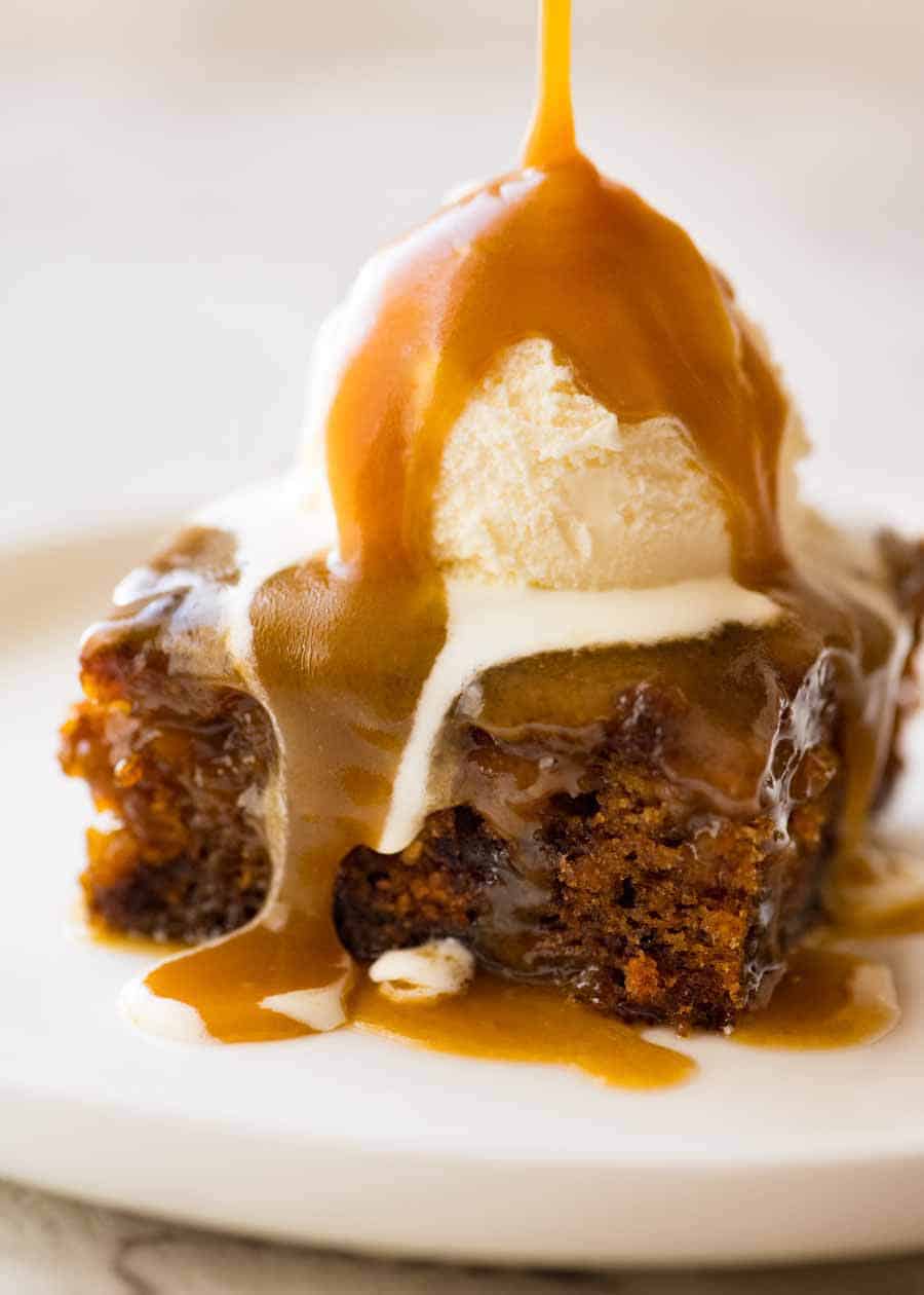 Warm butterscotch sauce being poured over Sticky Date Pudding topped with ice cream