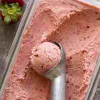Creamy No Churn Strawberry Ice Cream in a glass dish being scooped with an ice cream scooper