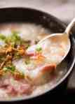 Close up of spoon scooping Chinese Ham Bone Rice Soup (Congee) out of a rustic brown bowl