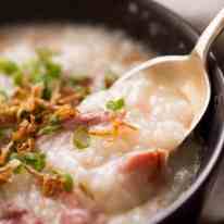 Close up of spoon scooping Chinese Ham Bone Rice Soup (Congee) out of a rustic brown bowl