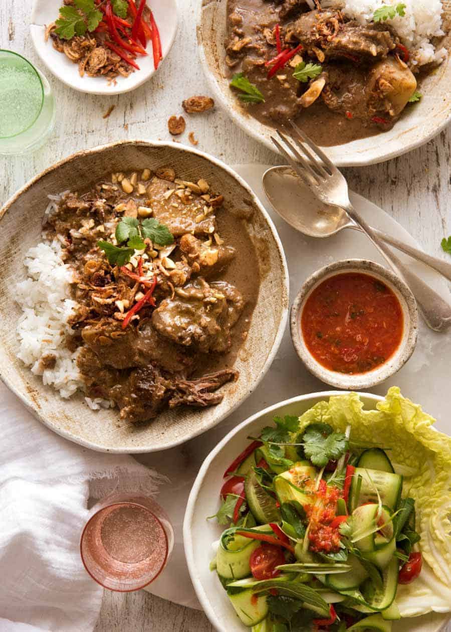 Overhead photo of two bowls with Massaman Curry on rice with a side salad, ready to be eaten