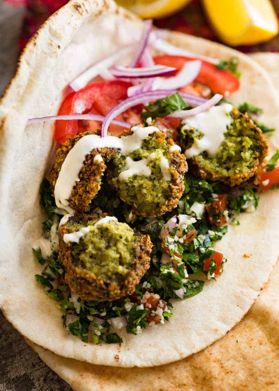 Close up of Falafel wrap in pita bread with tabbouleh, tomato, onion, hummus and tahini sauce