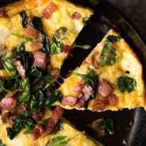 Overhead photo of Frittata with Bacon and Spinach in a black skillet, fresh out of the oven