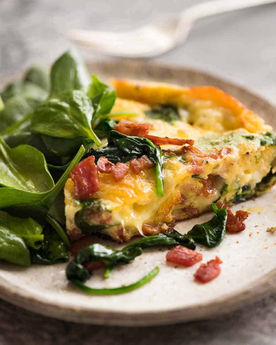 Slice of Frittata with Bacon and Spinach on a plate with a side of salad, ready to be eaten