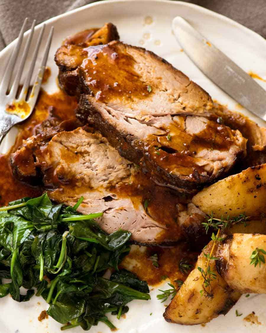 Slices of Slow Cooker Pork Loin Roast on a plate with wilted spinach and roast potatoes