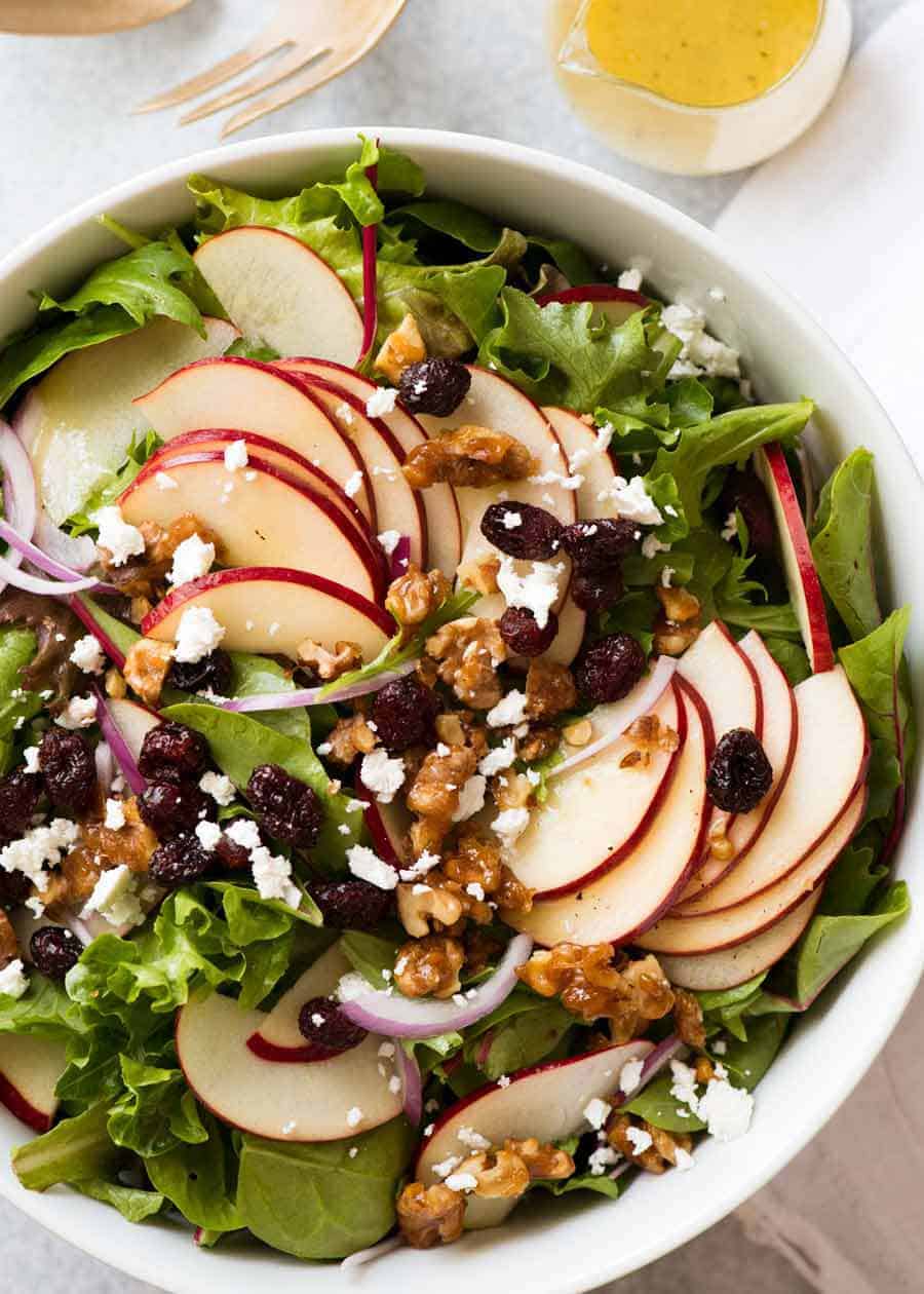 Overhead photograph  of Apple Salad with Candied Walnuts and Cranberries with vinaigrette dressing connected  the side