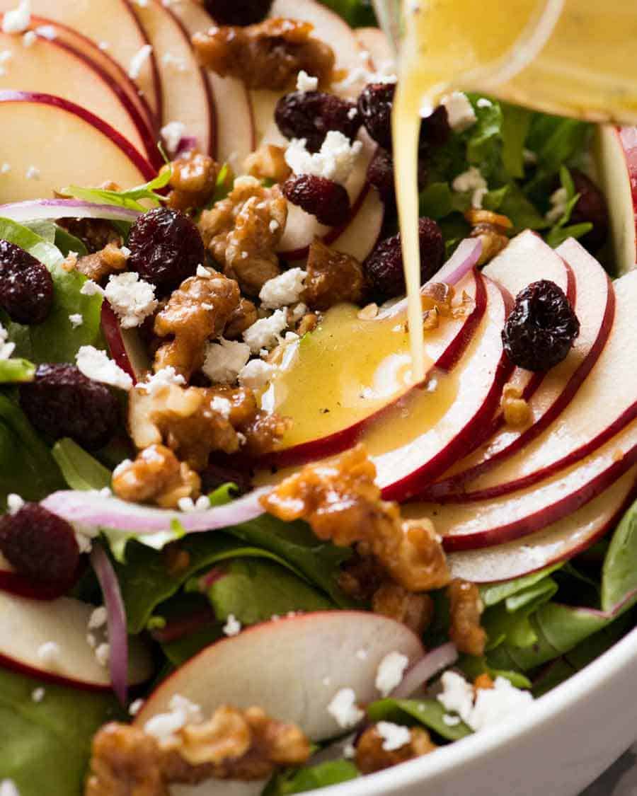 Vinaigrette being poured over Apple Salad with Candied Walnuts and Cranberries