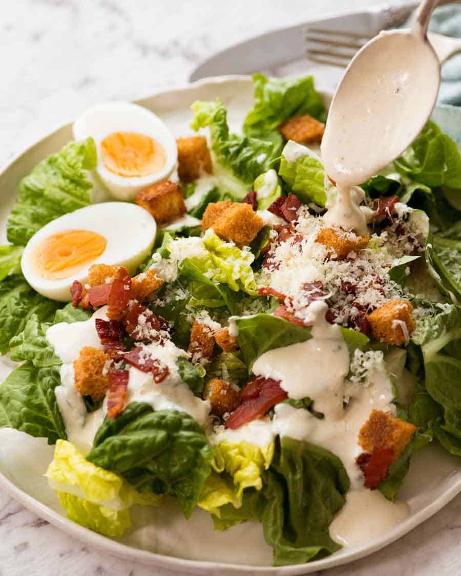 Spoon drizzling Healthy Caesar salad Yogurt Dressing on salad