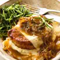 French Onion Smothered Pork Chops on mashed potato with a side of sautéed snow pea sprouts