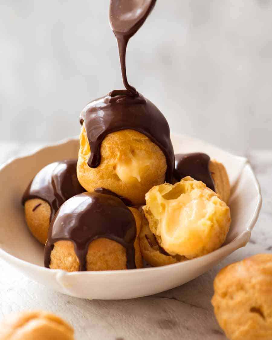 Spoon drizzling melted chocolate over profiteroles