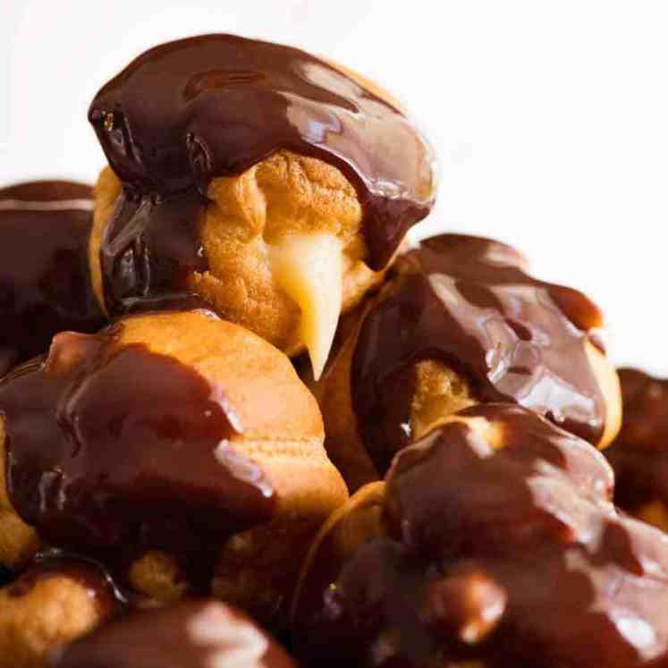 Close up of a pile of profiteroles filled with custard and drizzled with chocolate