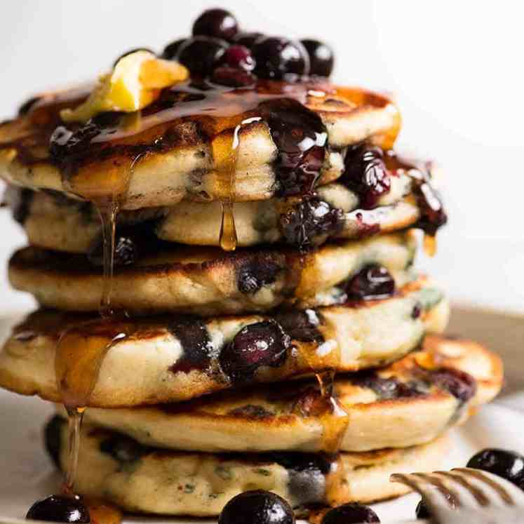 Stack of Fluffy Blueberry Pancakes dripping with maple syrup and melted butter
