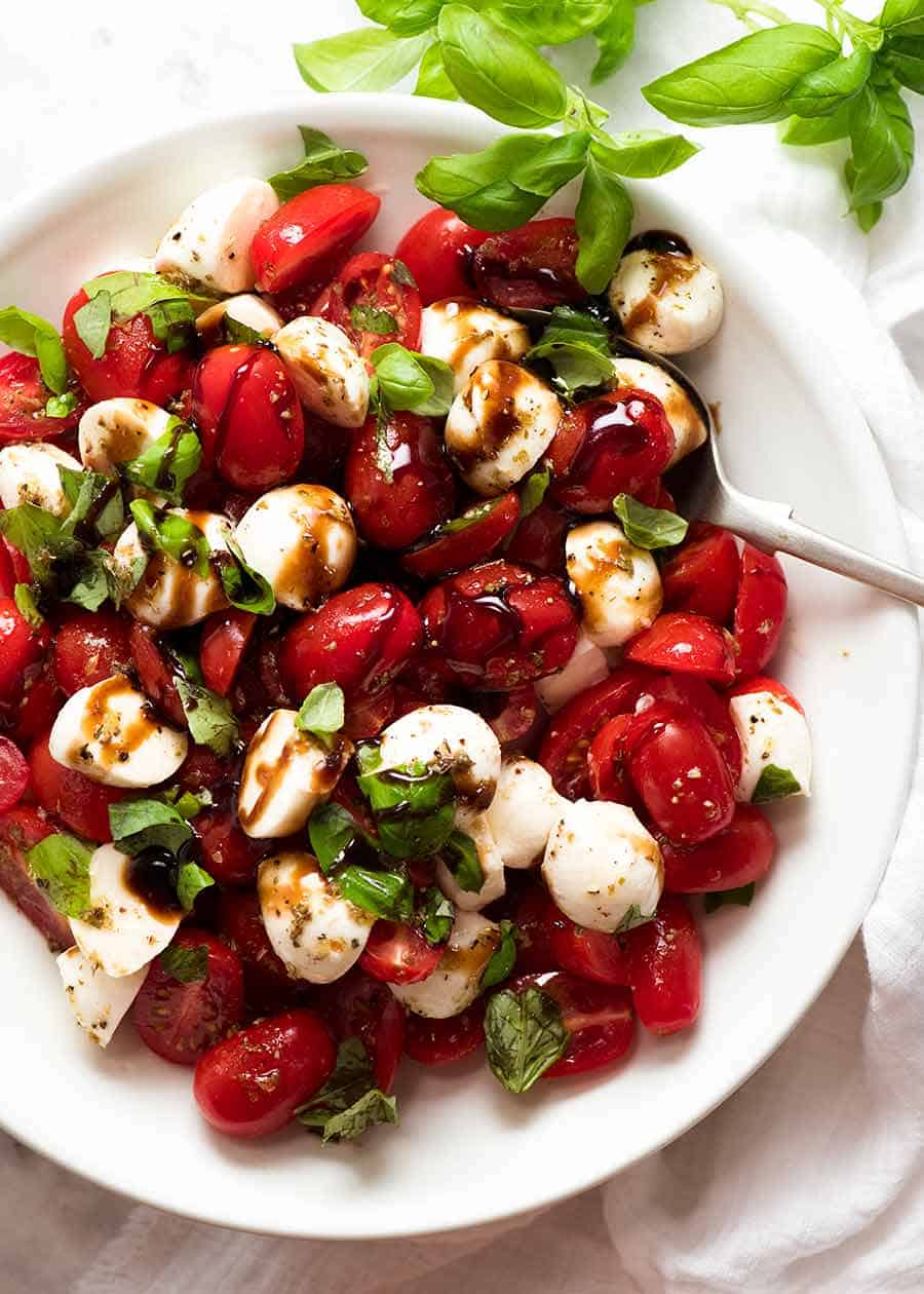 Overhead photo of Caprese Salad with cherry tomatoes, baby mozzarella / bocconcini, basil leaves and dressed with a garlic-herb Caprese Salad dressing and drizzled with balsamic glaze.