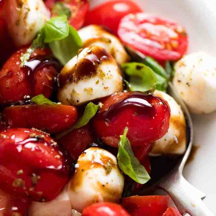 Close up of Caprese Salad with cherry tomatoes, baby mozzarella / bocconcini, basil leaves and dressed with a garlic-herb Caprese Salad dressing and drizzled with balsamic glaze.