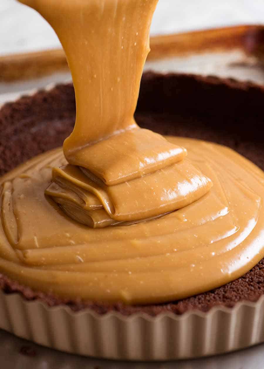 Peanut butter caramel filling being poured into cookie crust