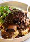 Close up of Slow Braised Beef Short Ribs in Red Wine Sauce on mashed potato on a rustic white plate, ready to be eaten