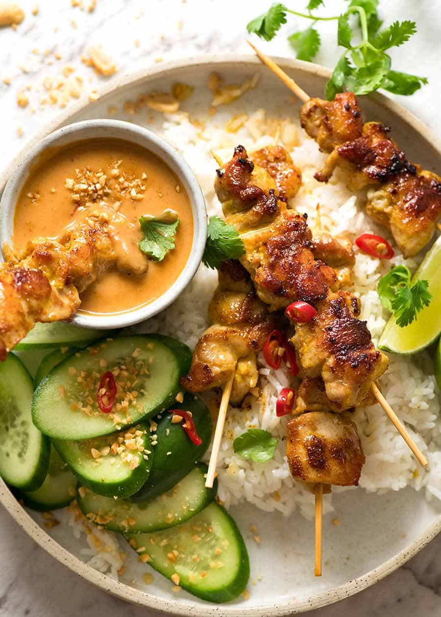 Overhead photo of Thai Chicken Satay with Thai Peanut Sauce on a plate with rice and cucumbers