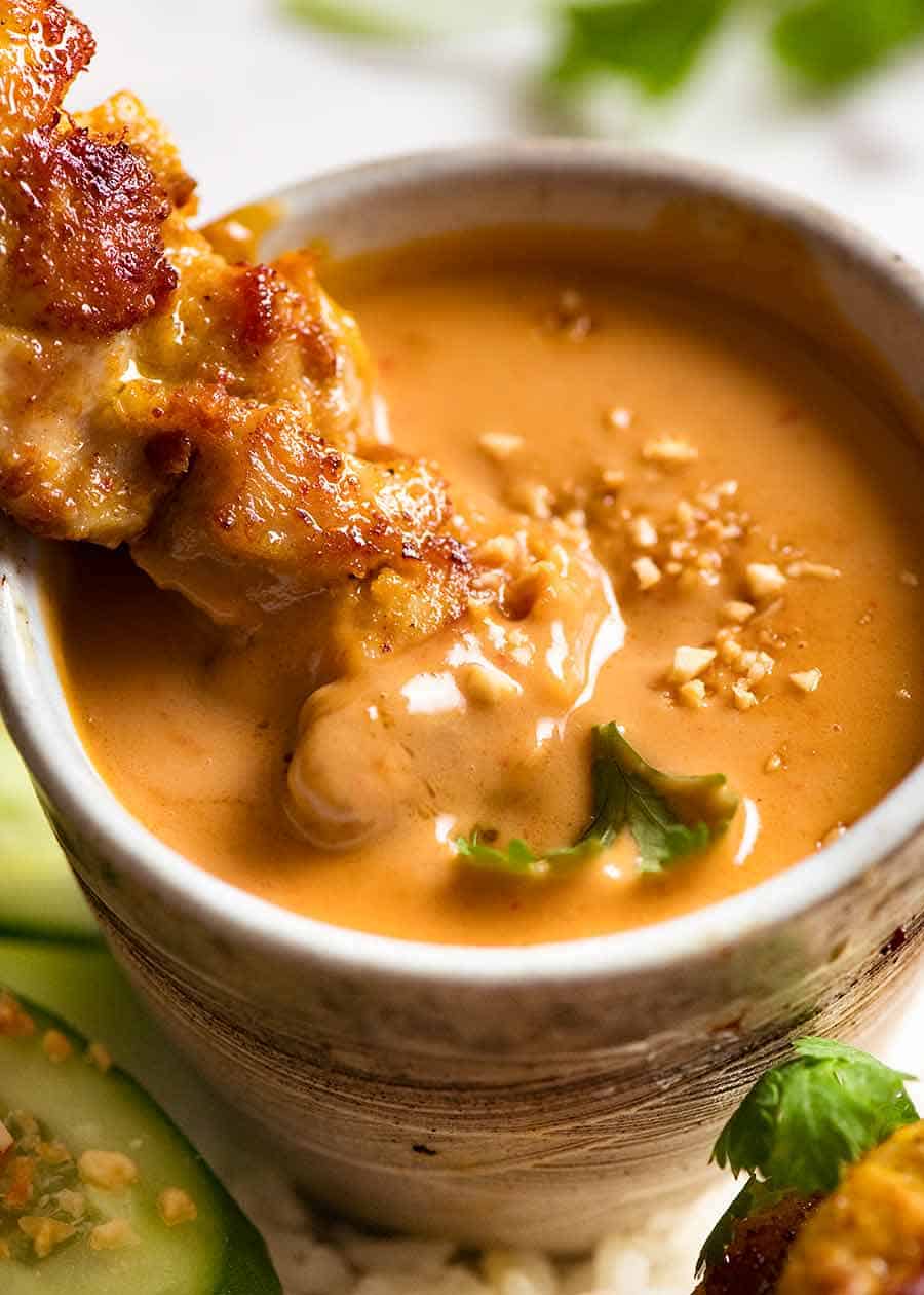 Close up of Thai Chicken Satay being dipped into Thai Peanut Sauce