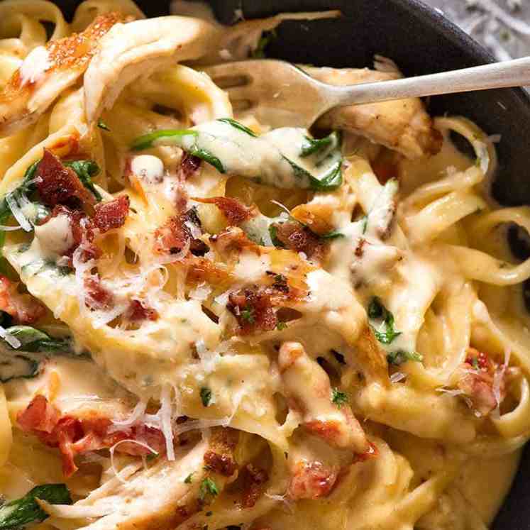 Close up of Chicken Pasta recipe with creamy alfredo sauce, sun dried tomato, spinach and bacon in a rustic black bowl, ready to be eaten