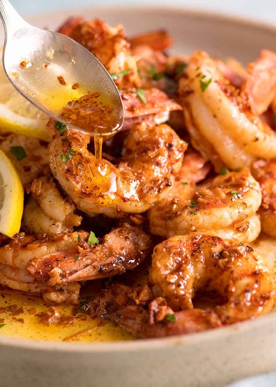 Close up of spoon drizzling Lemon Garlic Butter Sauce over grilled shrimp / prawns