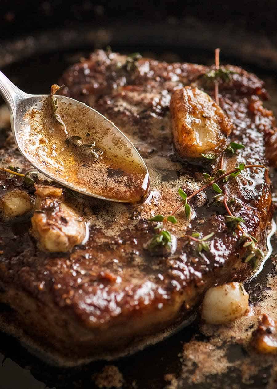 Close up of spoon drizzling browned garlic thyme butter sauce over steak