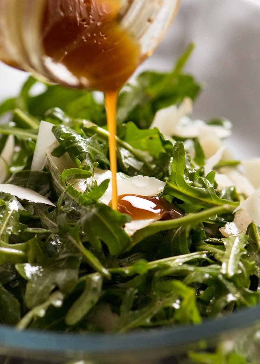 Close up of Balsamic Dressing being drizzled over rocket salad with shaved parmesan