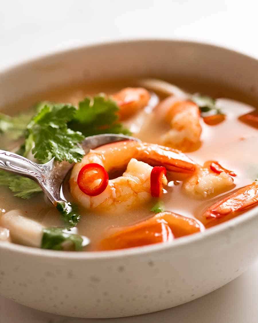 White bowl with Tom Yum Soup (Thai soup) with prawns / shrimp, mushrooms, tomato and garnished with coriander and chilli