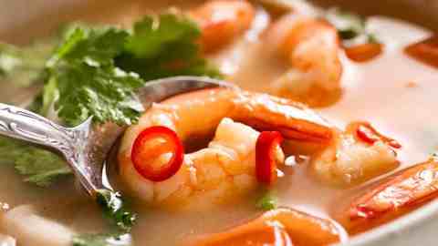 White bowl with Tom Yum Soup (Thai soup) with prawns / shrimp, mushrooms, tomato and garnished with coriander and chilli