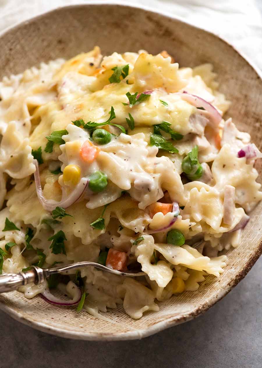 Close up of creamy baled pasta with bow ties, chicken, frozen peas corn and carrots