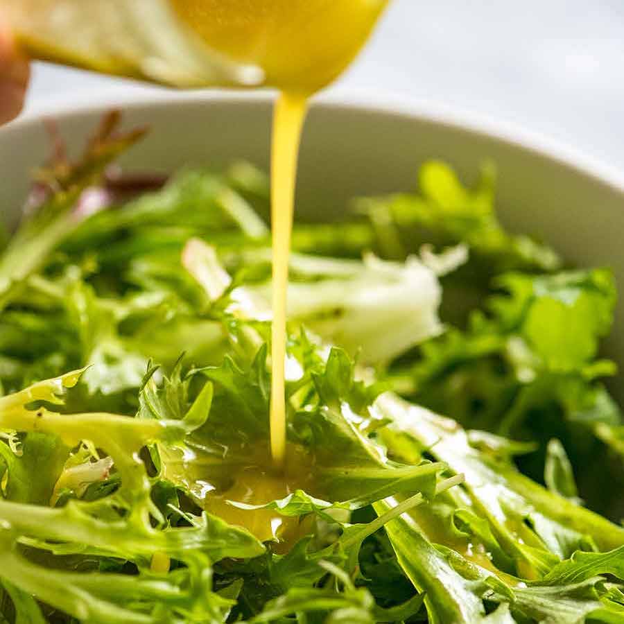 Close up pouring Salad Dressing over leafy green salad