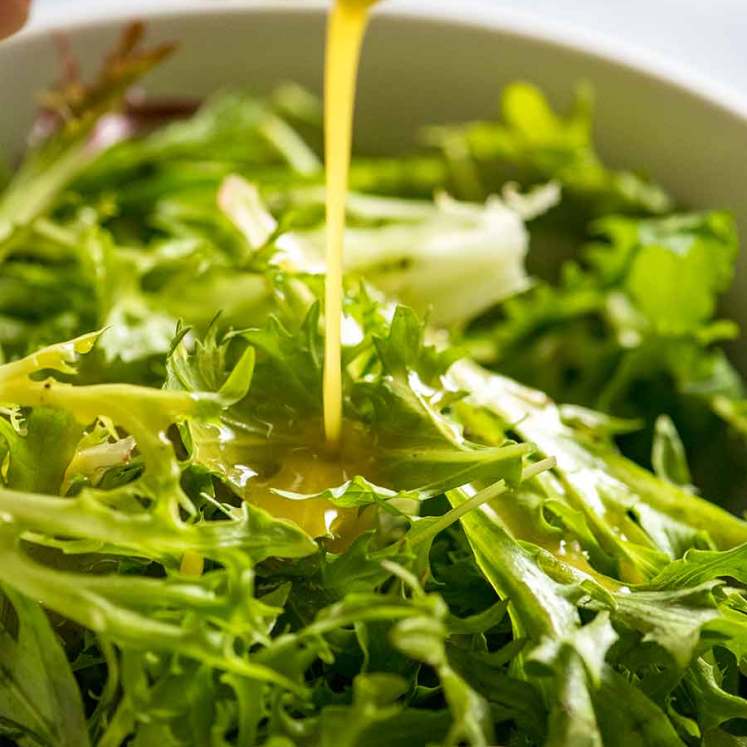 Pouring salad dressing over leafy salad