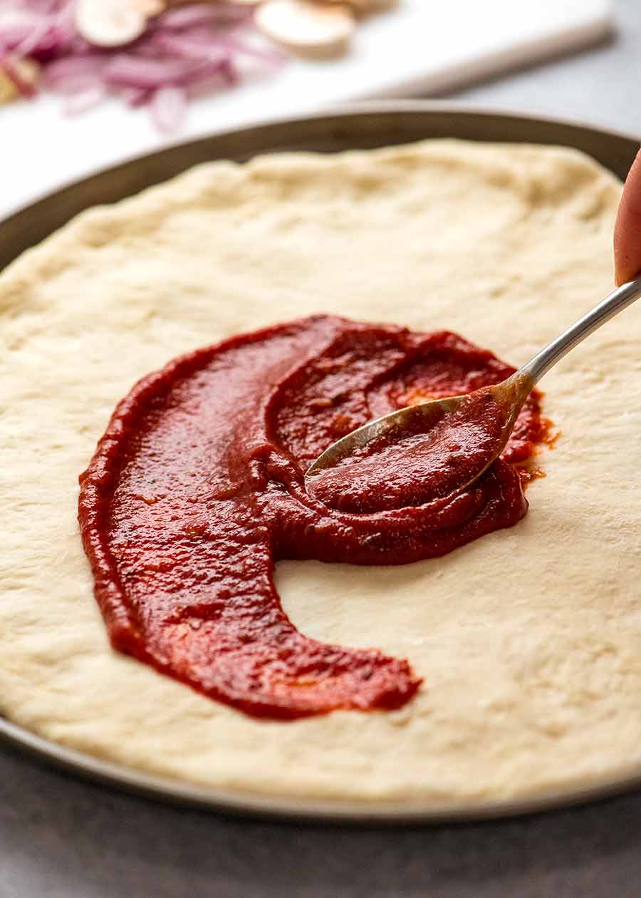 Spreading pizza sauce on homemade pizza crust