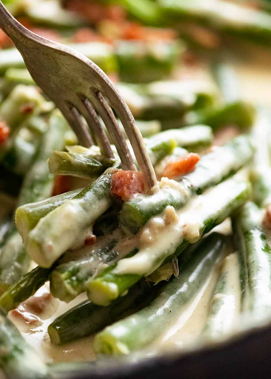 Close up of fork picking up creamy green beans