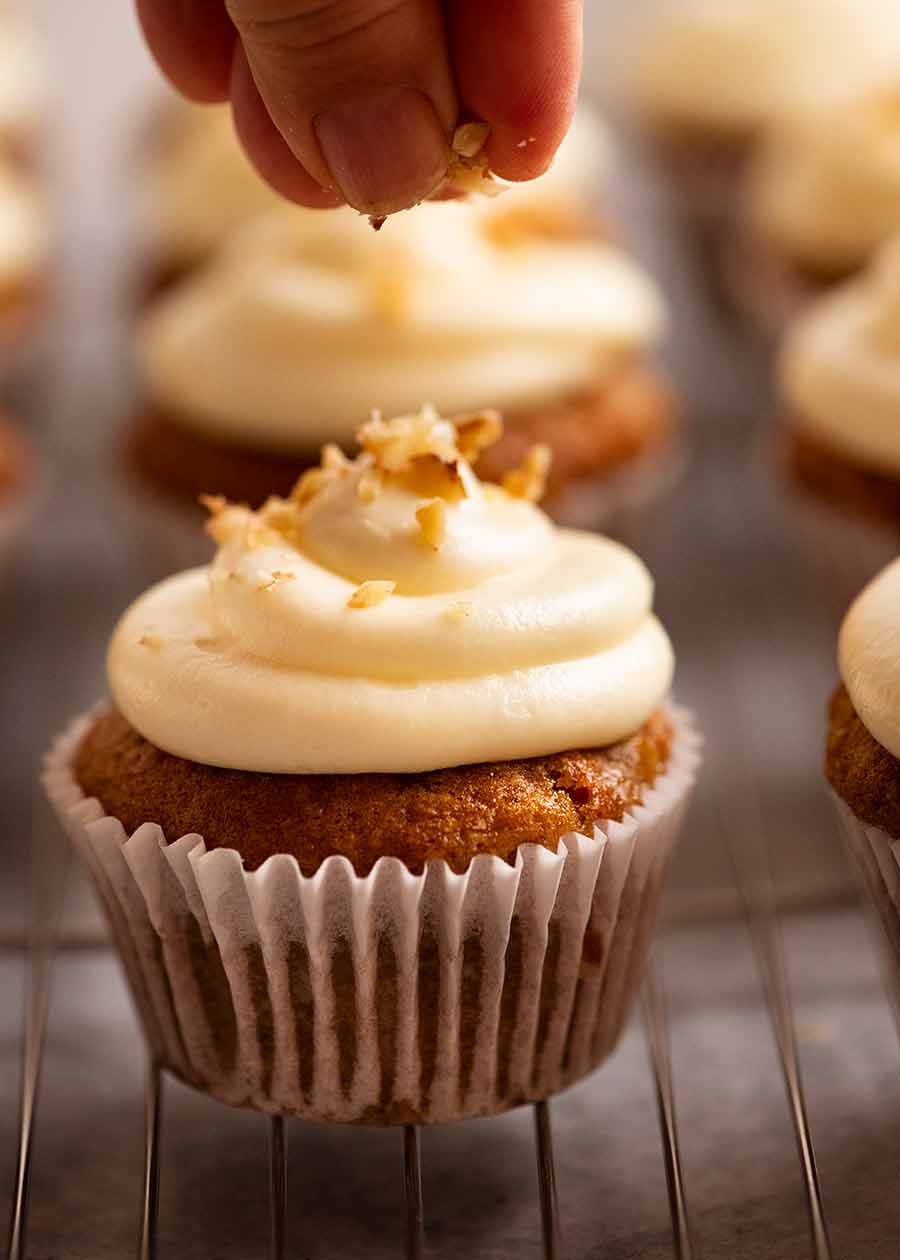 Hand sprinkling chopped pecans onto Carrot Cake Cupcakes with Cream Cheese Frosting