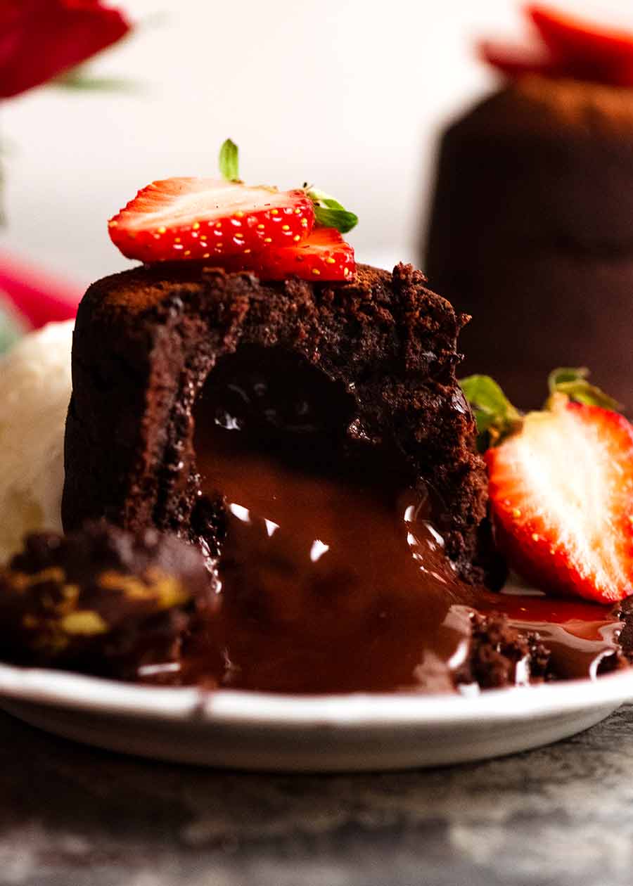 Close up of Molten Chocolate Cake with chocolate lava pouring out, decorated with strawberries