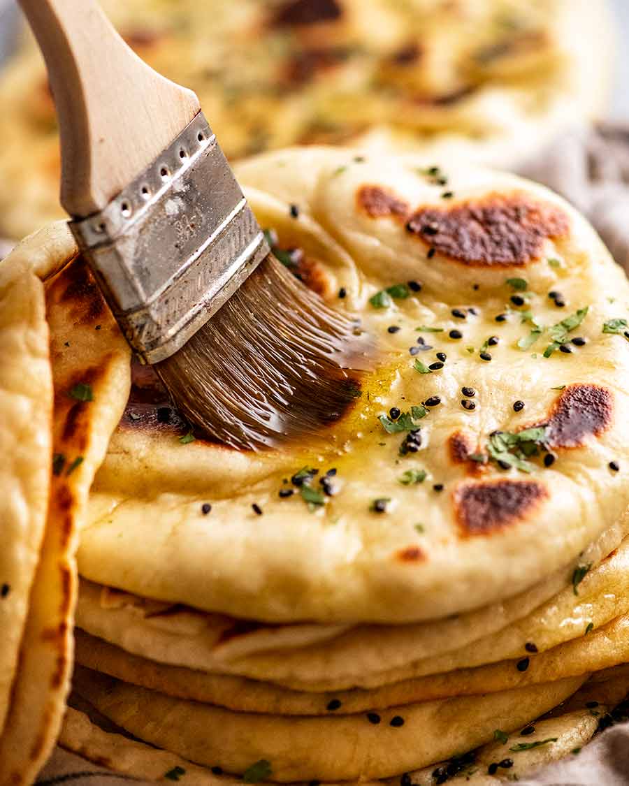 Brushing melted garlic butter on a freshly cooked naan