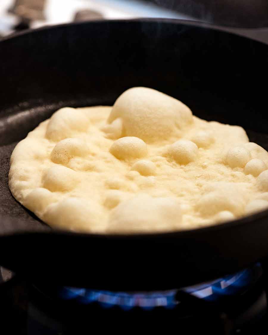 Bubbly puffy naan being cooked in a hot skillet