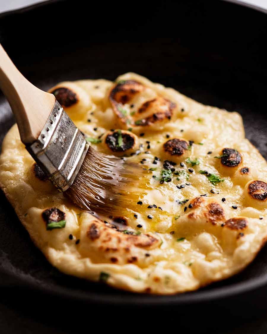 Burshing melted garlic butter on a freshly cooked naan in a hot cast iron skillet