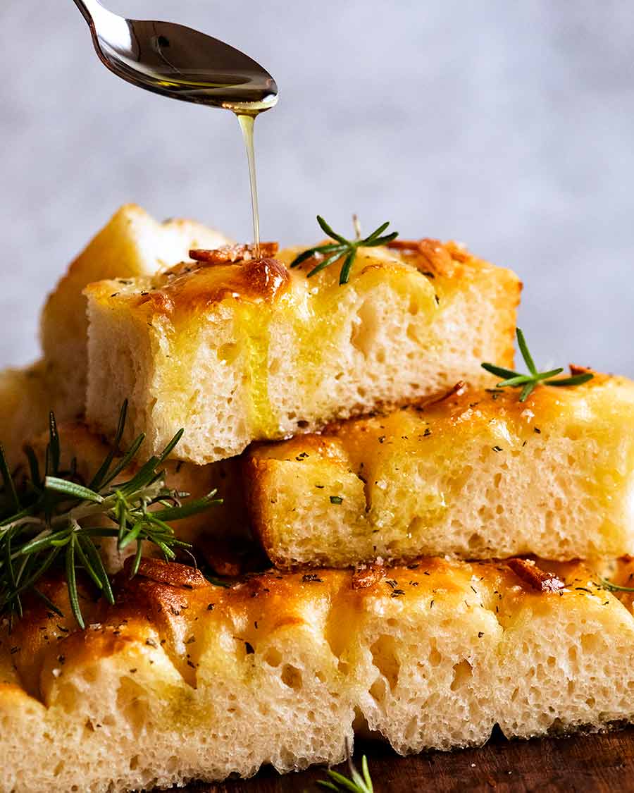 Drizzling a pile of warm focaccia with extra virgin olive oil