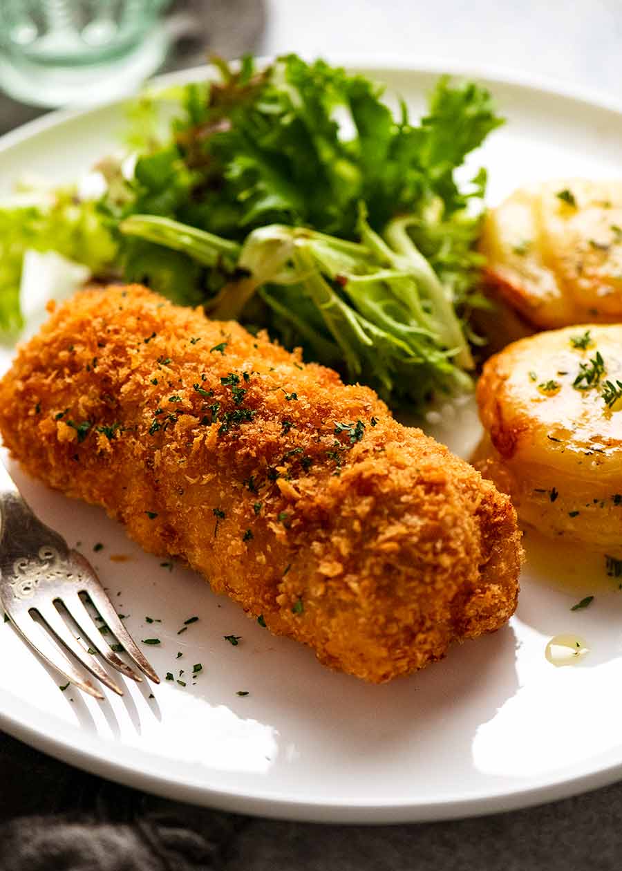 Chicken Kiev on a plate with a side of potato and salad