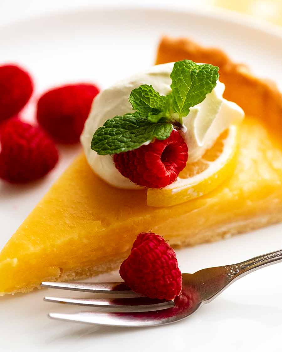 Close up photo of French Lemon Tart on a plate decorated with creme fraiche and raspberries
