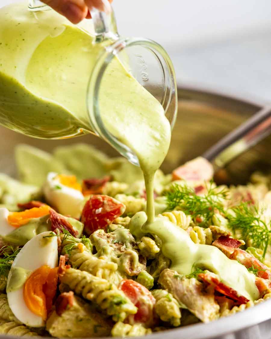 Pouring Avocado Ranch Dressing over chicken pasta salad